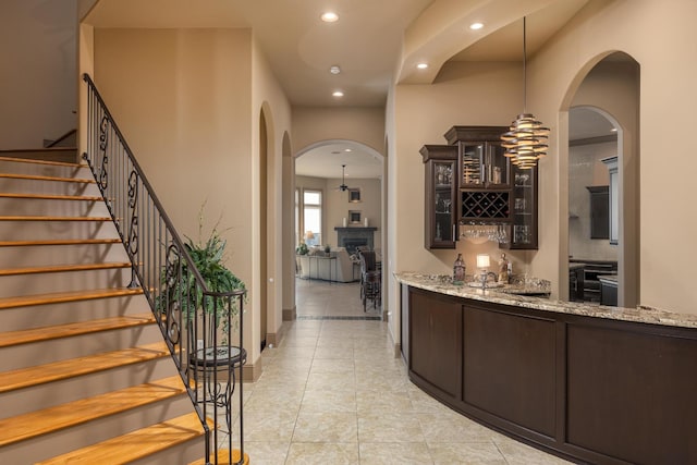 bar with light tile patterned flooring, light stone countertops, dark brown cabinetry, and decorative light fixtures