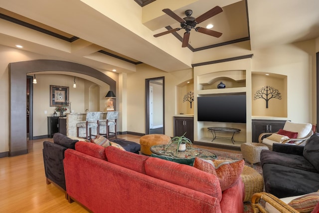 living room featuring built in features, ornamental molding, light hardwood / wood-style floors, and ceiling fan