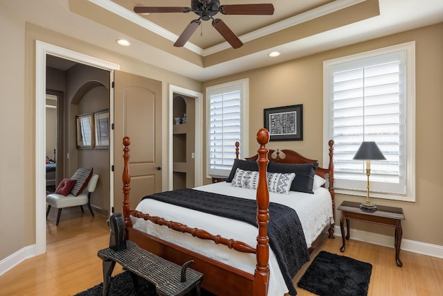 bedroom featuring ornamental molding, a raised ceiling, multiple windows, and light hardwood / wood-style flooring