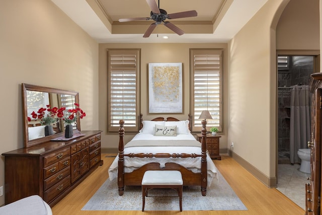 bedroom with multiple windows, light wood-type flooring, and a tray ceiling