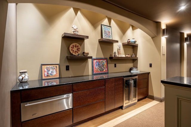 bar featuring dark brown cabinets, beverage cooler, and light wood-type flooring