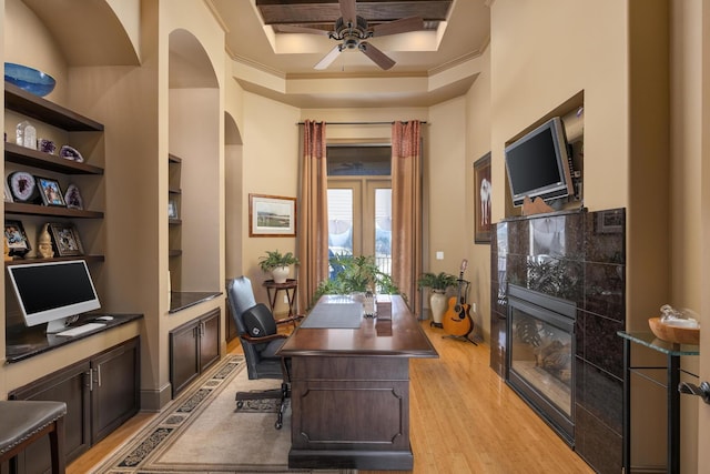 office space featuring crown molding, light hardwood / wood-style flooring, a tile fireplace, ceiling fan, and a tray ceiling