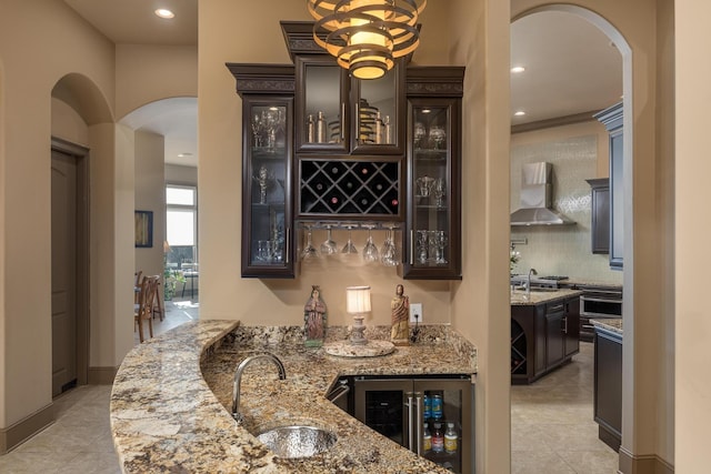 bar with sink, wall chimney range hood, beverage cooler, and light stone counters