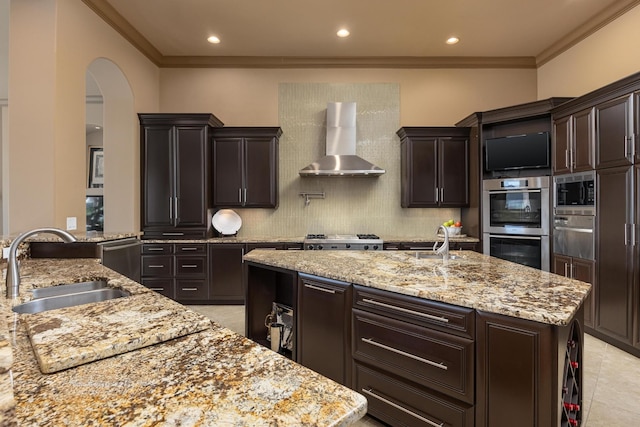 kitchen featuring appliances with stainless steel finishes, wall chimney exhaust hood, sink, and a kitchen island with sink