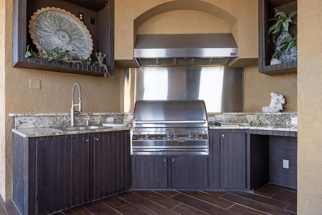 kitchen featuring sink, light stone counters, dark brown cabinetry, and wall chimney exhaust hood