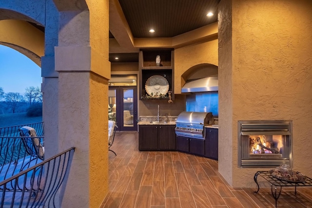 patio terrace at dusk featuring an outdoor fireplace, a grill, sink, and area for grilling