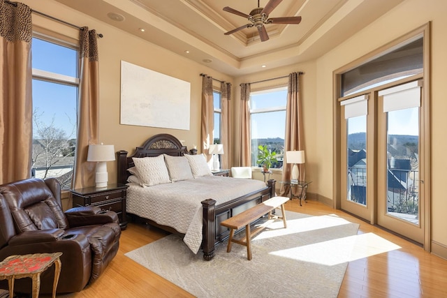 bedroom featuring multiple windows, access to outside, a raised ceiling, and light wood-type flooring