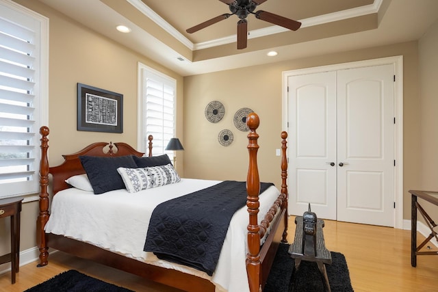 bedroom with light wood-type flooring, ornamental molding, a tray ceiling, a closet, and ceiling fan