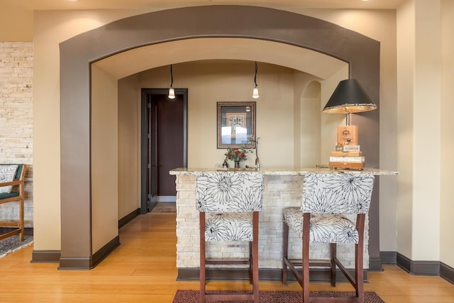 bar with hanging light fixtures, light stone countertops, and light wood-type flooring