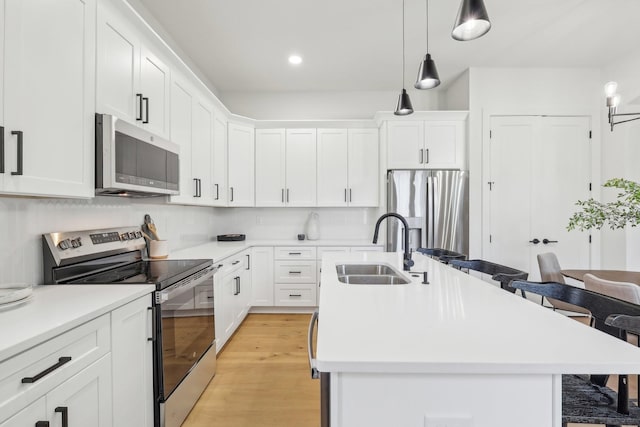 kitchen with appliances with stainless steel finishes, a breakfast bar, decorative light fixtures, sink, and white cabinets