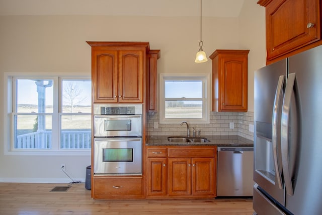 kitchen featuring tasteful backsplash, sink, dark stone countertops, light hardwood / wood-style floors, and stainless steel appliances