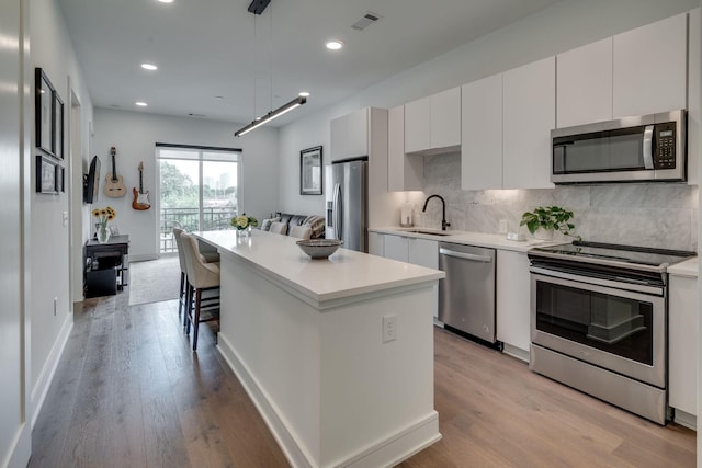 kitchen with sink, white cabinetry, a kitchen island, pendant lighting, and stainless steel appliances