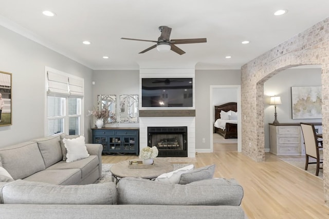 living room with ceiling fan, a large fireplace, ornamental molding, and light hardwood / wood-style floors