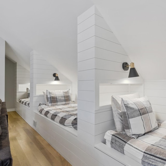 bedroom featuring light hardwood / wood-style flooring, wood walls, and vaulted ceiling