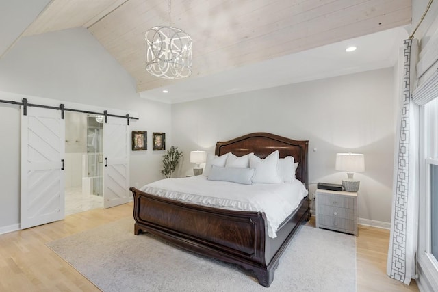 bedroom featuring an inviting chandelier, lofted ceiling, a barn door, ensuite bath, and light hardwood / wood-style flooring