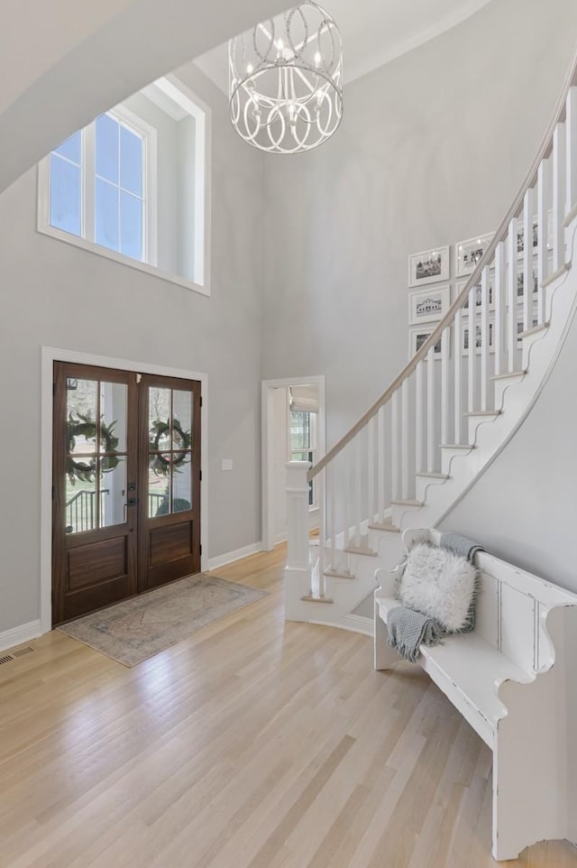 entryway featuring french doors, light hardwood / wood-style floors, a high ceiling, and a notable chandelier