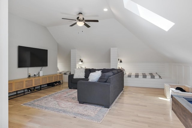 living room featuring ceiling fan, vaulted ceiling with skylight, and light hardwood / wood-style flooring