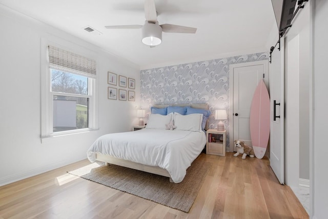 bedroom featuring ceiling fan, a barn door, and light hardwood / wood-style floors