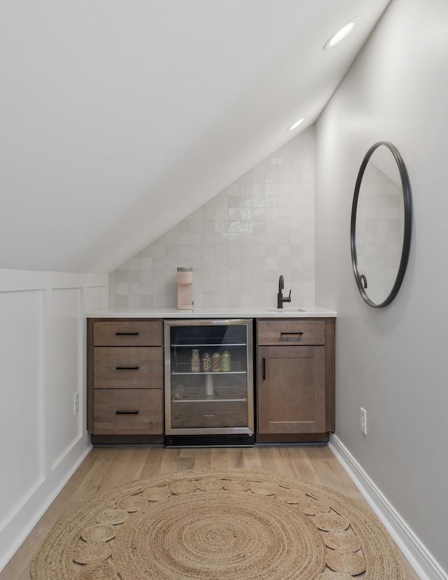 bar featuring vaulted ceiling, light hardwood / wood-style floors, and beverage cooler