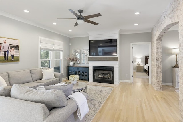 living room with crown molding, light hardwood / wood-style floors, a large fireplace, and ceiling fan