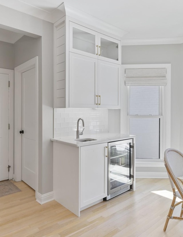 bar with wine cooler, sink, white cabinetry, tasteful backsplash, and light wood-type flooring