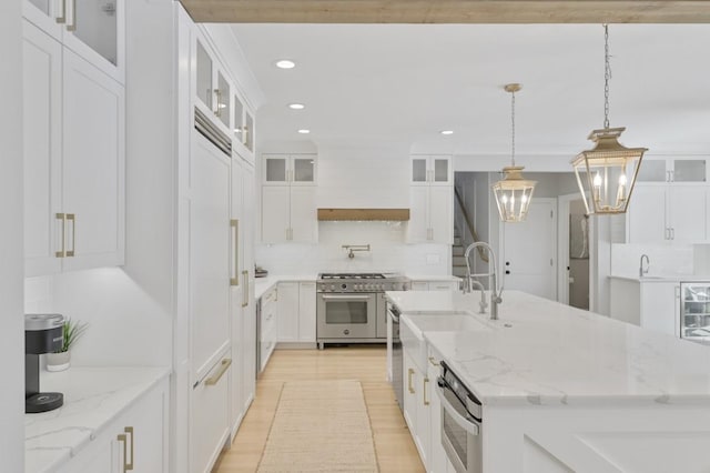 kitchen with pendant lighting, light stone countertops, a kitchen island with sink, range with two ovens, and white cabinets