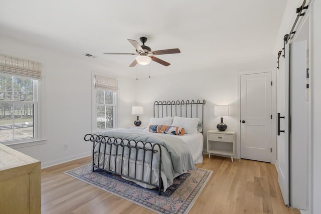 bedroom with multiple windows, light hardwood / wood-style floors, and a barn door