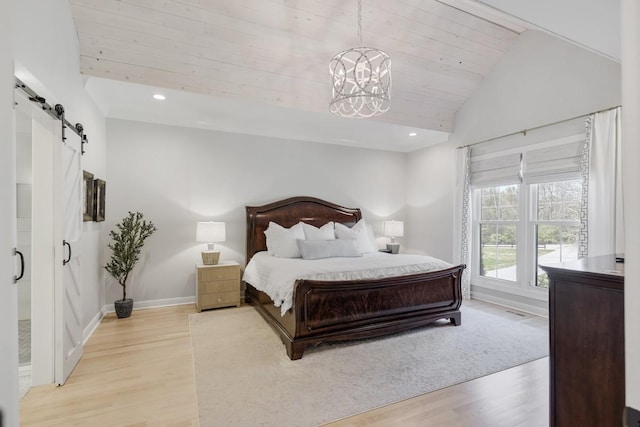 bedroom featuring an inviting chandelier, a barn door, light hardwood / wood-style floors, and vaulted ceiling