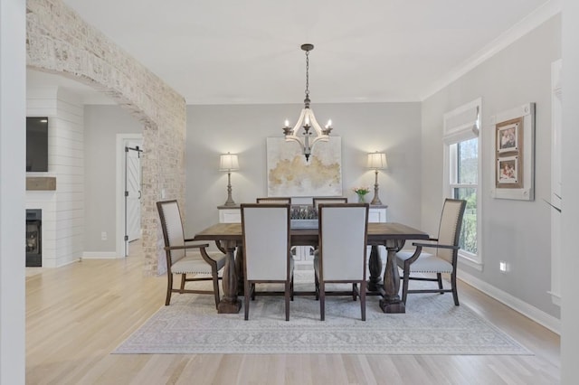 dining space featuring an inviting chandelier, a fireplace, light hardwood / wood-style flooring, and ornamental molding