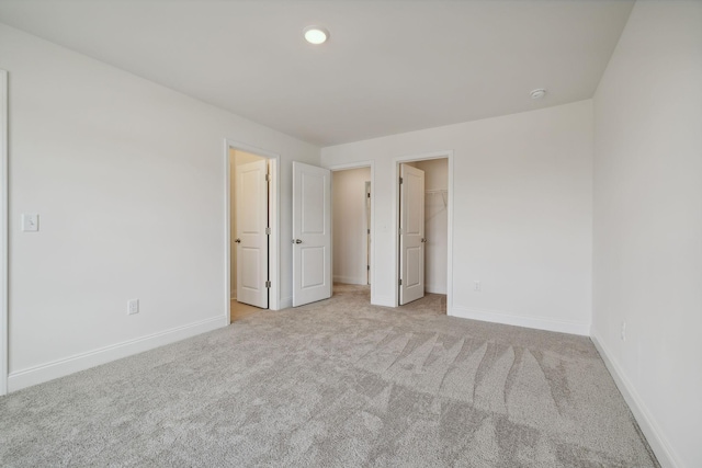 unfurnished bedroom featuring light carpet and a walk in closet