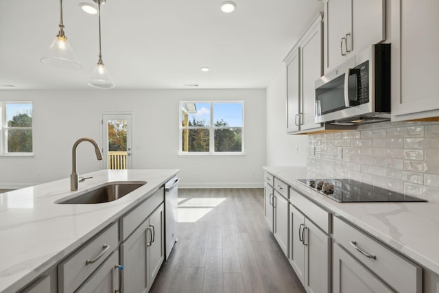 kitchen with appliances with stainless steel finishes, sink, gray cabinetry, hanging light fixtures, and light stone counters