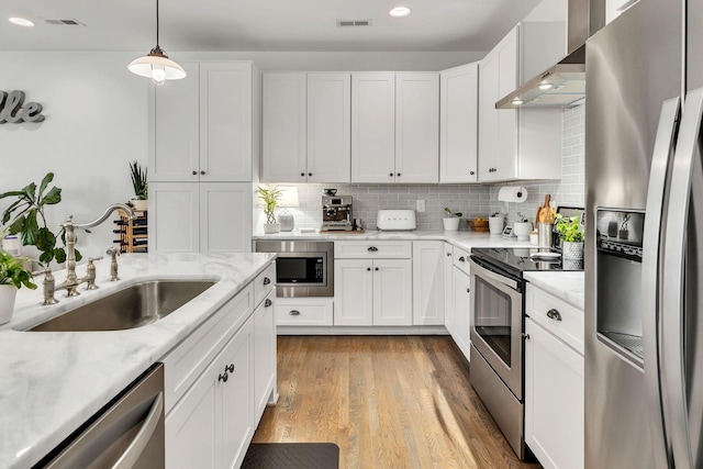 kitchen with sink, white cabinetry, decorative light fixtures, stainless steel appliances, and wall chimney range hood