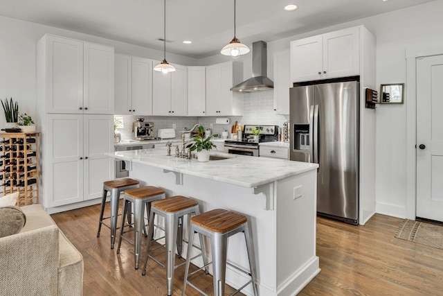 kitchen with appliances with stainless steel finishes, a center island with sink, white cabinets, and wall chimney exhaust hood