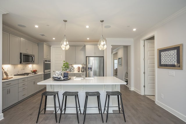 kitchen with gray cabinetry, pendant lighting, stainless steel appliances, and an island with sink