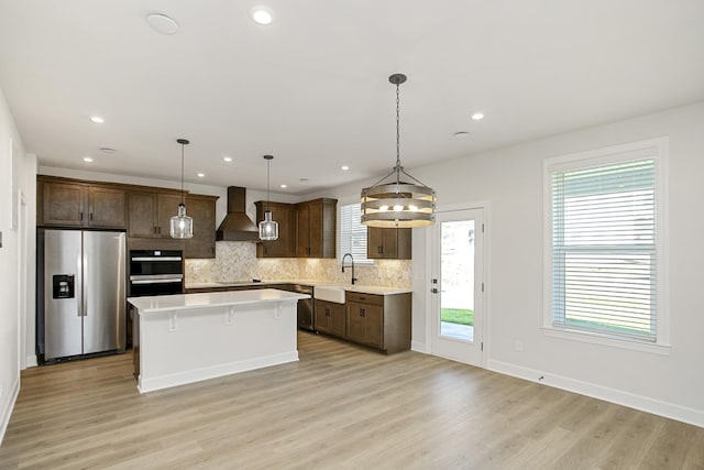 kitchen with sink, a center island, black appliances, custom range hood, and decorative light fixtures