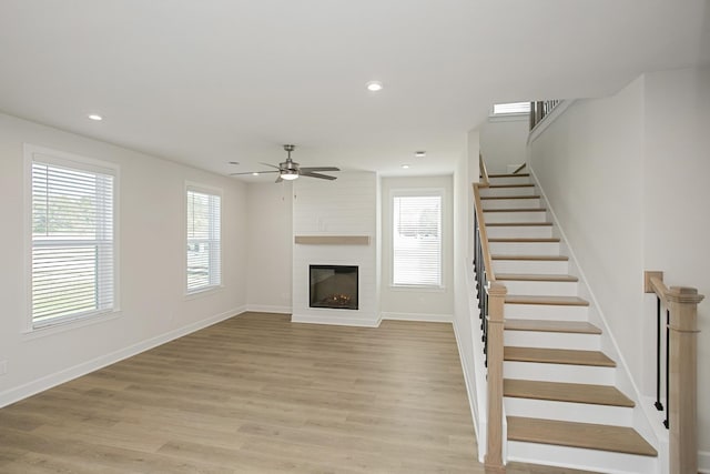 unfurnished living room with a large fireplace, a wealth of natural light, ceiling fan, and light hardwood / wood-style flooring