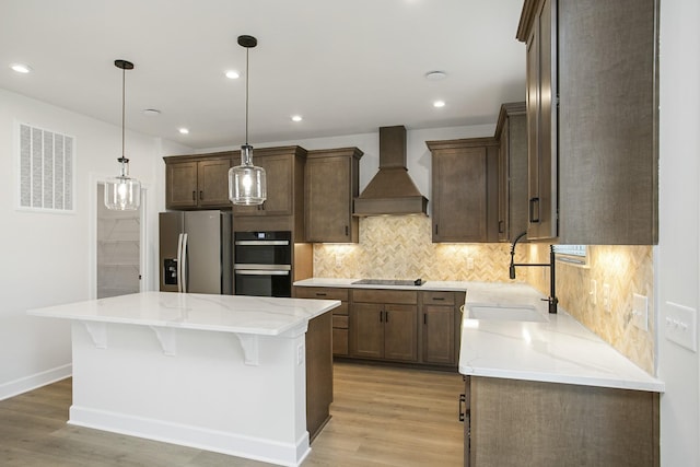 kitchen featuring a kitchen island, sink, custom exhaust hood, hanging light fixtures, and black appliances