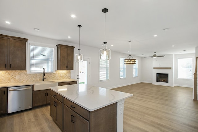 kitchen featuring pendant lighting, sink, light stone counters, and stainless steel dishwasher