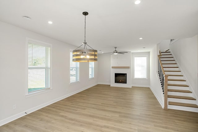 unfurnished living room with ceiling fan, a large fireplace, and light wood-type flooring