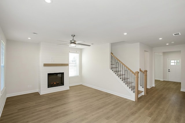 unfurnished living room with wood-type flooring, a large fireplace, and ceiling fan