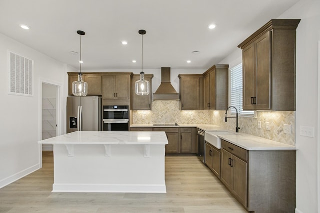 kitchen with sink, a center island, black appliances, custom range hood, and decorative light fixtures