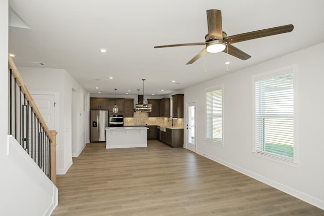 kitchen with hanging light fixtures, dark brown cabinets, a kitchen island, stainless steel fridge with ice dispenser, and wall chimney exhaust hood