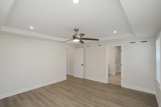 empty room featuring a raised ceiling, wood-type flooring, ornamental molding, and ceiling fan