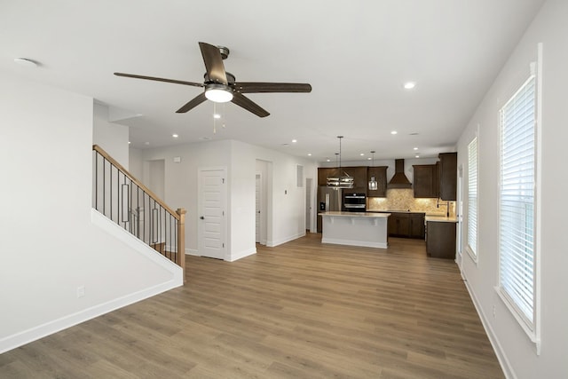 kitchen with hardwood / wood-style flooring, hanging light fixtures, a center island, and wall chimney range hood