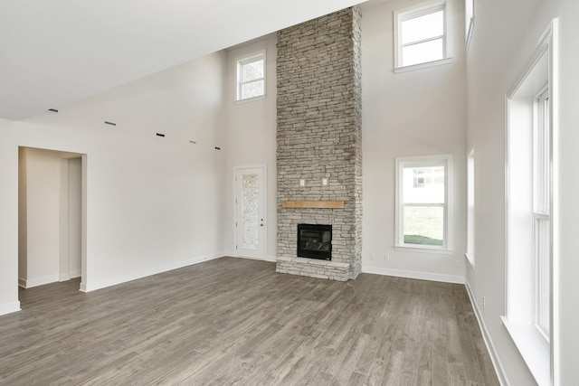 unfurnished living room featuring a towering ceiling, a stone fireplace, and hardwood / wood-style floors