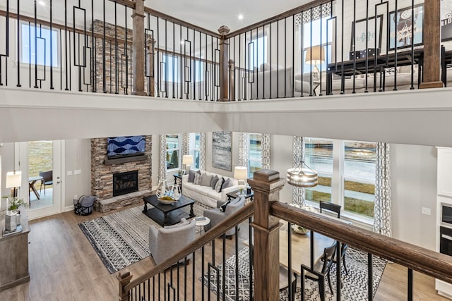 living room featuring a towering ceiling, plenty of natural light, a stone fireplace, and hardwood / wood-style floors