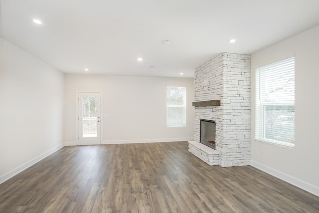 unfurnished living room with a stone fireplace, a wealth of natural light, and dark hardwood / wood-style floors