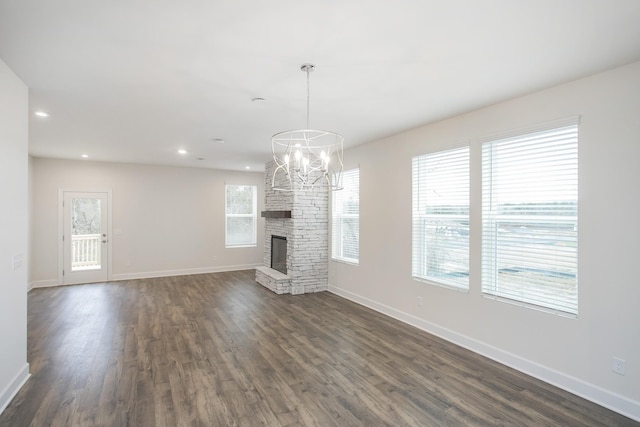 unfurnished living room featuring a stone fireplace, dark wood-type flooring, and a chandelier