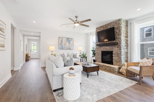 living room with dark wood-type flooring, ceiling fan, and a stone fireplace