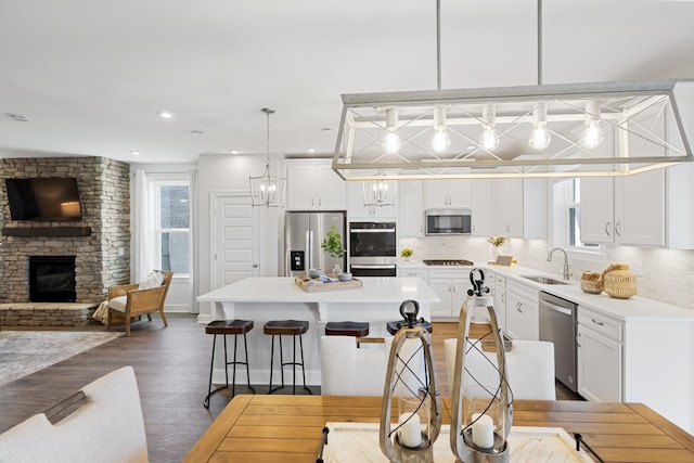 kitchen with a stone fireplace, a breakfast bar area, white cabinets, hanging light fixtures, and stainless steel appliances